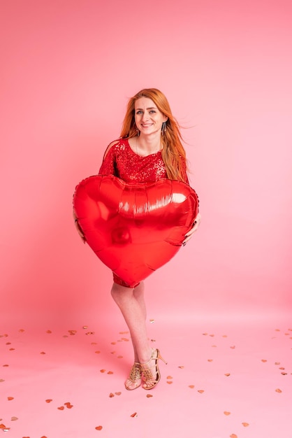 Hermosa chica pelirroja con globo de corazón rojo posando concepto de feliz día de San Valentín