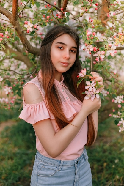 Hermosa chica pelirroja en la primavera en las ramas del manzano