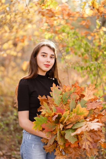 Hermosa chica pelirroja con un ramo de hojas amarillas de otoño