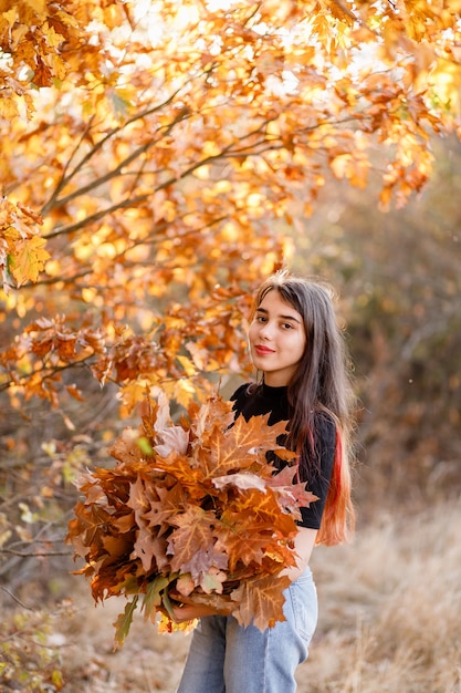 Hermosa chica pelirroja con un ramo de hojas amarillas de otoño