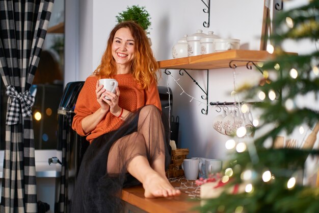 Una hermosa chica pelirroja se sienta en la tela para techos en una elegante y acogedora cocina decorada para Navidad