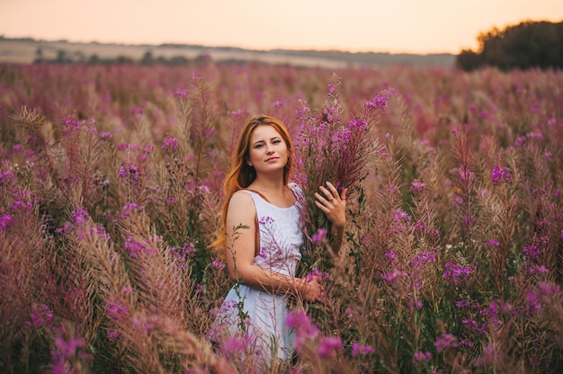 Hermosa chica pelirroja con un vestido en un campo de flores de té de sauce.