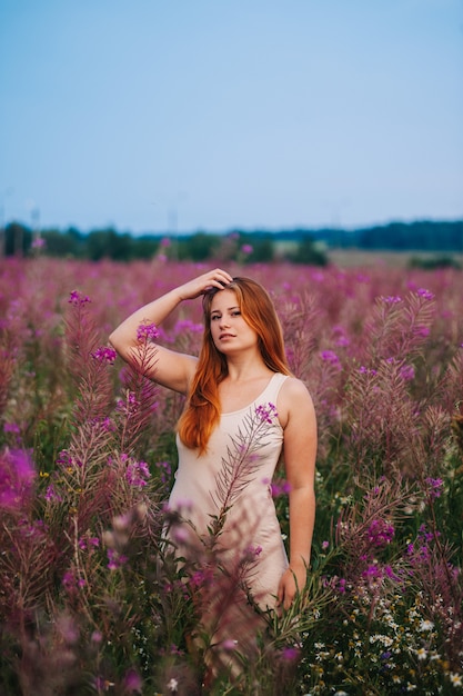 Hermosa chica pelirroja con un vestido en un campo de flores de té de sauce.