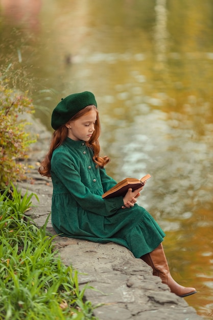 hermosa chica pelirroja con un vestido verde y dar un paseo en el otoño en el parque con un libro