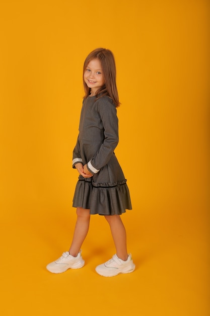 hermosa chica de pelo castaño en un vestido gris de la escuela fondo amarillo