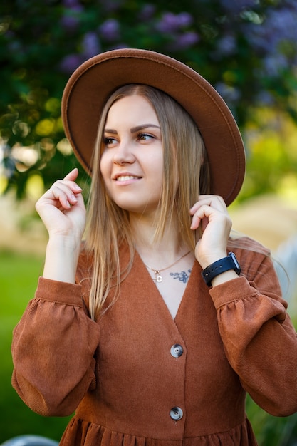 Hermosa chica de pelo largo bien formada en el sombrero sobre un fondo de flores lilas