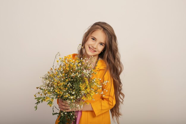 hermosa chica de pelo largo en un impermeable amarillo con flores silvestres de otoño en sus manos