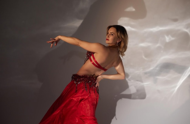 Hermosa chica con el pelo largo y negro con un vestido oriental rojo bailando danza del vientre en la sala de estudio Cultura árabe