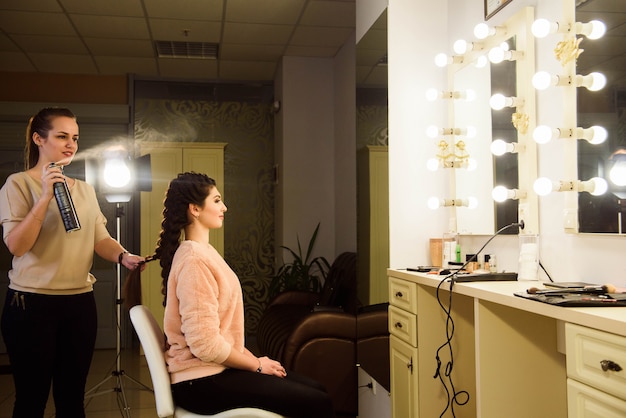 Hermosa chica con el pelo largo, peluquero teje una trenza francesa, en un salón de belleza. Cuidado profesional del cabello y creación de peinados.