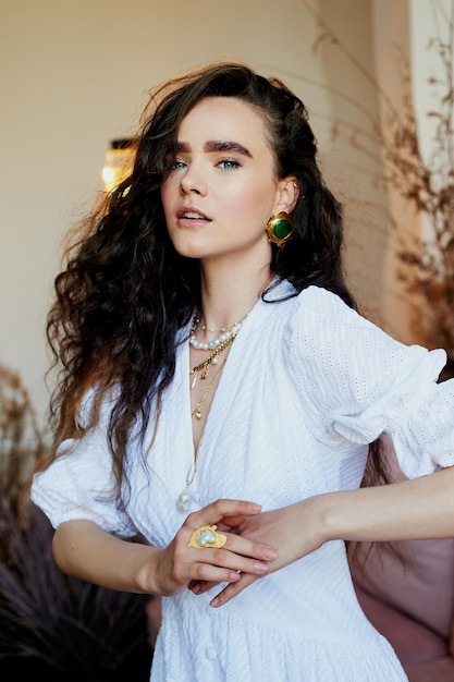 Una hermosa chica con el pelo largo y rizado con un vestido largo blanco se mueve dinámicamente Estudio fotográfico con cereales Moda y belleza