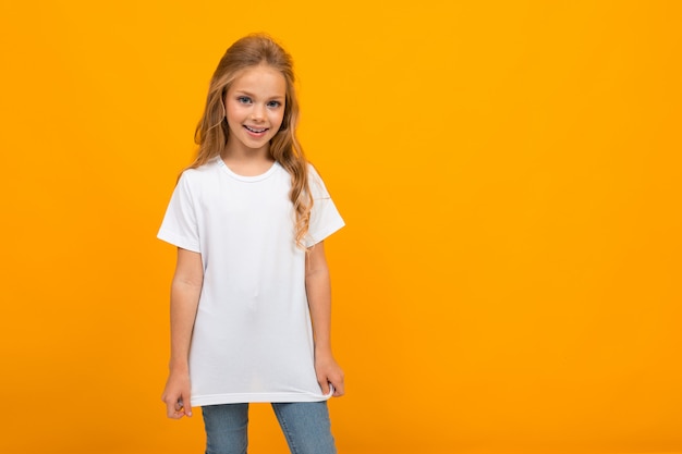 Hermosa chica con el pelo largo y rubio sobre un fondo amarillo en una camiseta blanca sin inscripciones