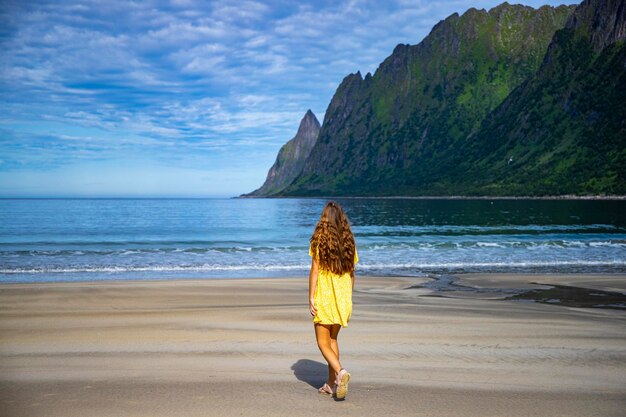 hermosa chica de pelo largo con vestido amarillo camina por la famosa playa ersfjordstranda, senja, noruega