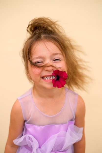 Hermosa chica de pelo rizado con flor de petunia en la boca sonríe dulcemente
