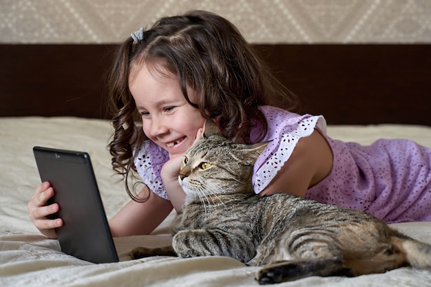 Hermosa chica de pelo rizado con un gato mirando la tableta