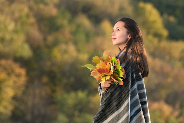 Hermosa chica pensativa con ramo de hojas de otoño