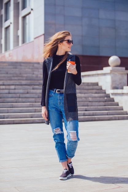 Hermosa chica de pie en la calle con café y vasos.