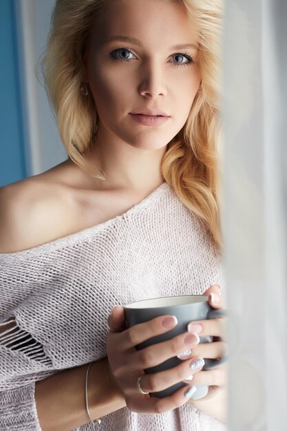 Hermosa chica de pie en casa con una taza de café