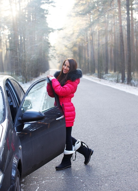 Hermosa chica de pie cerca del auto y se inclina contra la puerta del auto