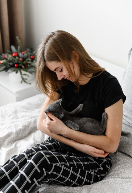 Hermosa chica en pijama sostiene a su amada mascota en sus brazos. Gatito escocés en brazos de la niña.