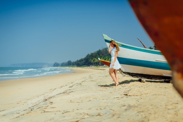 Hermosa chica en la playa tropical cerca del barco de los pescadores.