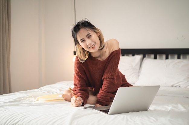 Hermosa chica que trabaja con la computadora portátil en la cama, trabaja desde el concepto de hogar