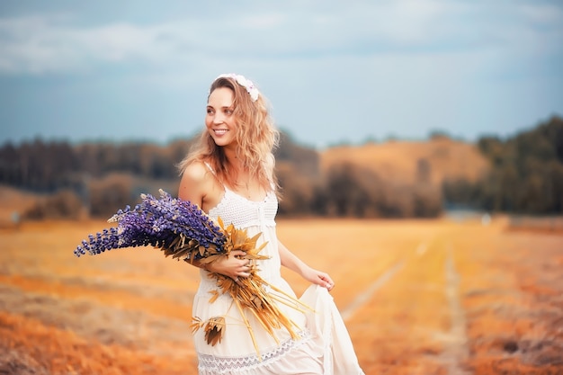 Hermosa chica con un ramo de flores azules en la naturaleza en otoño