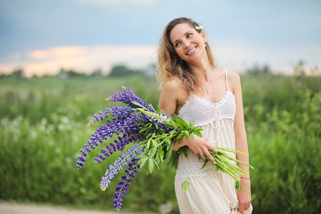 Hermosa chica con un ramo de flores azules en la naturaleza en verano