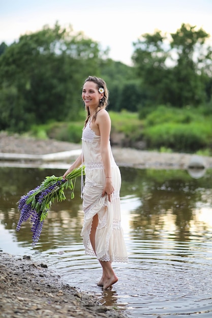 Hermosa chica con un ramo de flores azules en la naturaleza en verano