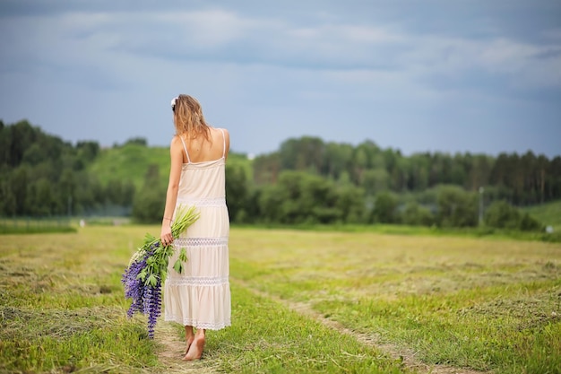 Hermosa chica con un ramo de flores azules en la naturaleza en verano