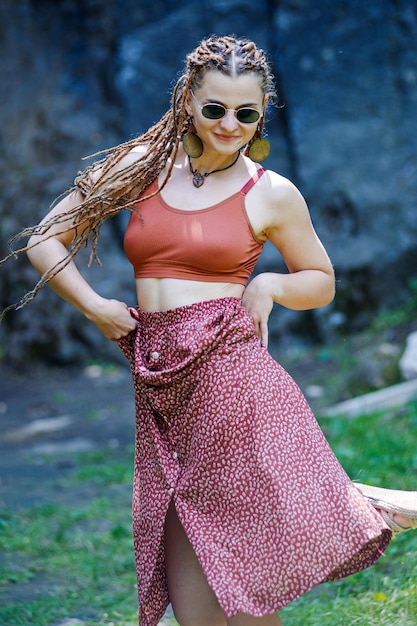 Hermosa chica con rastas vestida estilo hippie posa al aire libre