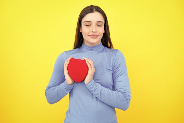 Hermosa chica con regalo de San Valentín sobre fondo amarillo Retrato de mujer joven sosteniendo rojo