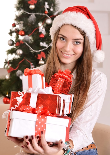 Hermosa chica con regalos cerca del árbol de Navidad con sombrero de santa