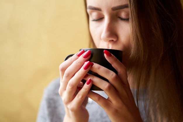 Foto hermosa chica con uñas rojas sosteniendo una taza de café.