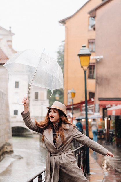 Hermosa chica romántica con abrigo y sombrero con paraguas transparente en Annecy. Francia. La chica del sombrero en Francia.