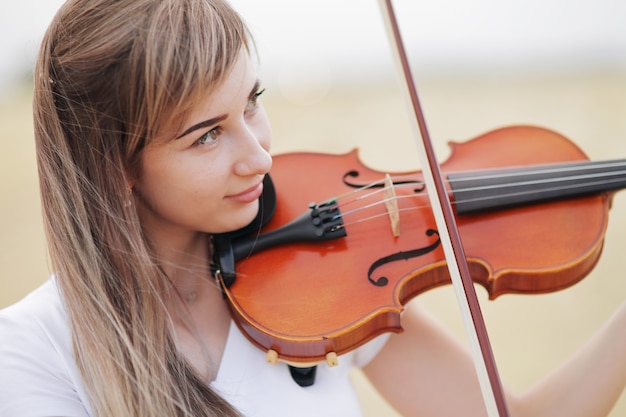 Hermosa chica romántica con cabello suelto tocando el violín en el campo después de la cosecha