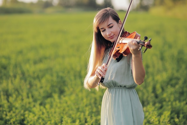 Hermosa chica romántica con cabello suelto tocando el violín en el campo después de la cosecha