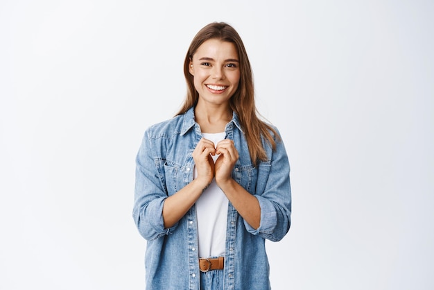 Hermosa chica romántica mostrando gesto de corazón Te amo firmar sonriendo feliz a la cámara de pie contra fondo blanco Copiar espacio