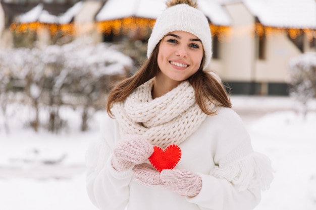 Hermosa chica en ropa blanca de invierno en la calle que tiene corazón para el día de San Valentín