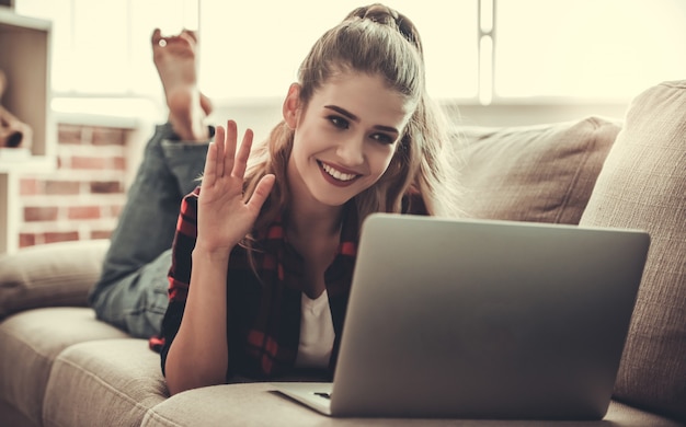 Hermosa chica en ropa casual está usando una computadora portátil.