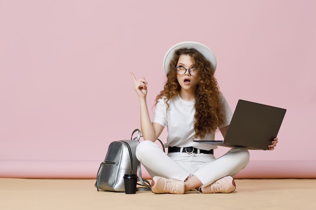 Hermosa chica en ropa casual y gafas sentada en el suelo y usando laptop