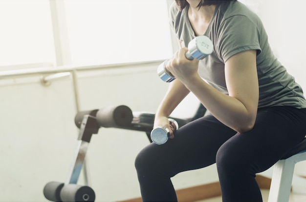 Hermosa chica en ropa deportiva ejercicio con mancuerna plantean en el gimnasio para tratar de perder peso