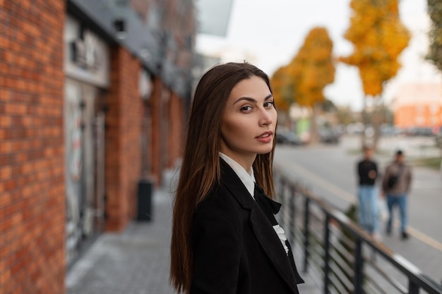 Hermosa chica con ropa elegante de negocios caminando por la ciudad y mirando a la cámara