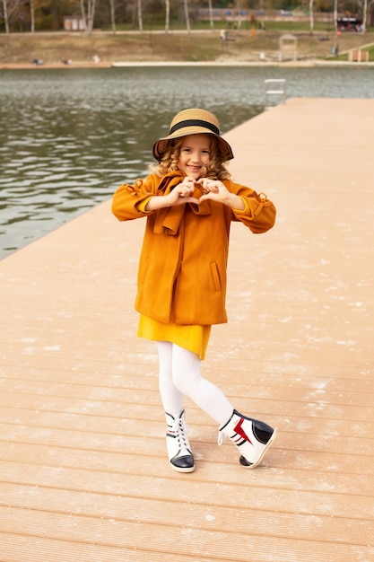 una hermosa chica rubia con un abrigo beige con un sombrero en el muelle de la ciudad lago naturaleza