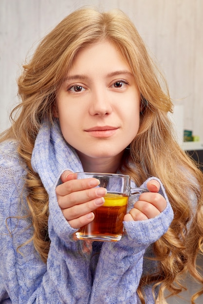 Hermosa chica rubia bebiendo té con limón en casa