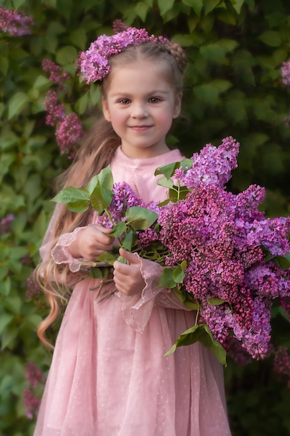 Una hermosa chica rubia con cabello largo sostiene un ramo de lilas en sus manos