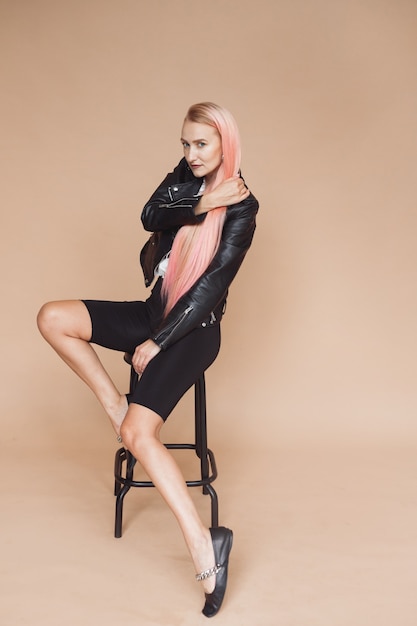 Hermosa chica rubia con chaqueta de cuero negro y cabello rosado en estilo rock sobre fondo liso