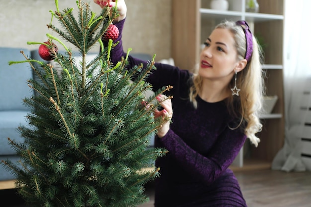 Hermosa chica rubia decora un pequeño árbol de Navidad natural en una olla