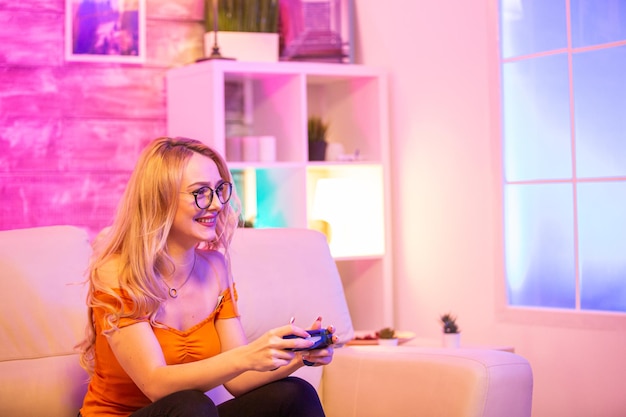 Hermosa chica rubia emocionada mientras juega videojuegos con controladores inalámbricos. Chica alegre jugando juegos de video.