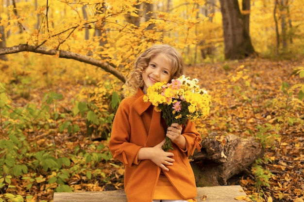 Hermosa chica rubia feliz con un abrigo beige en el parque de la ciudad de otoño