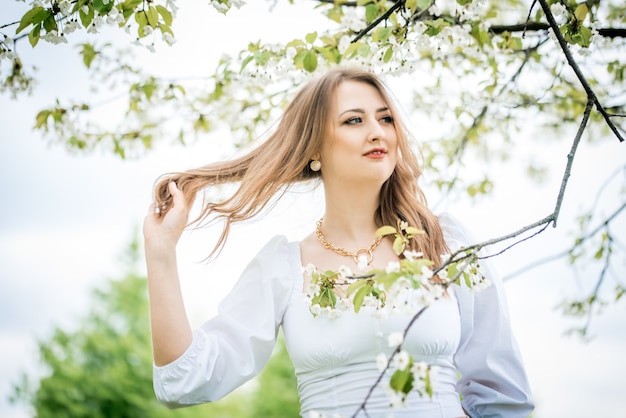 Hermosa chica rubia en jardín de cerezos de primavera.